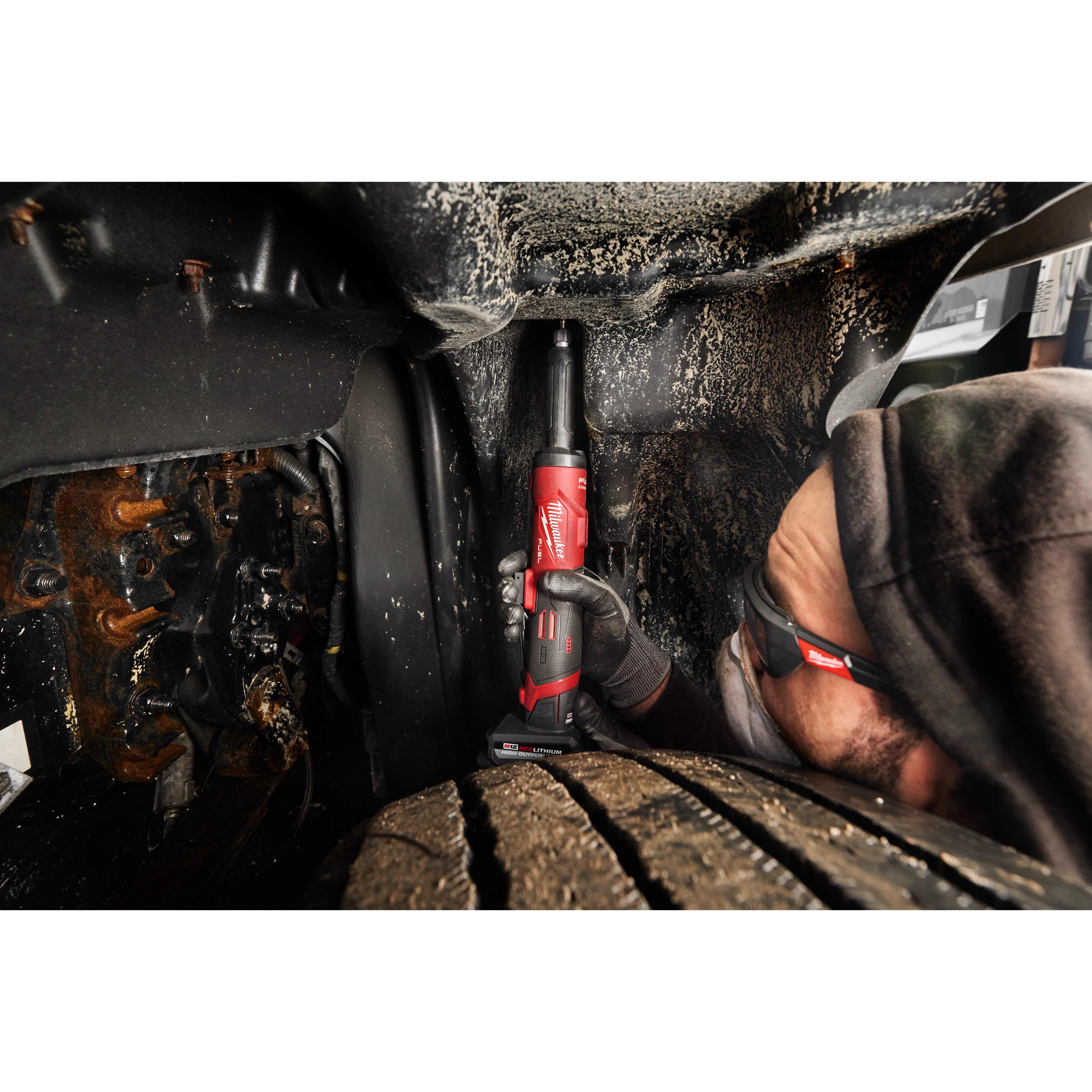 Worker using M12 FUEL 1/4" Extended Die Grinder in a tight vehicle wheel well space.