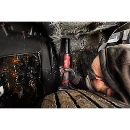 Worker using M12 FUEL 1/4" Extended Die Grinder in a tight vehicle wheel well space.