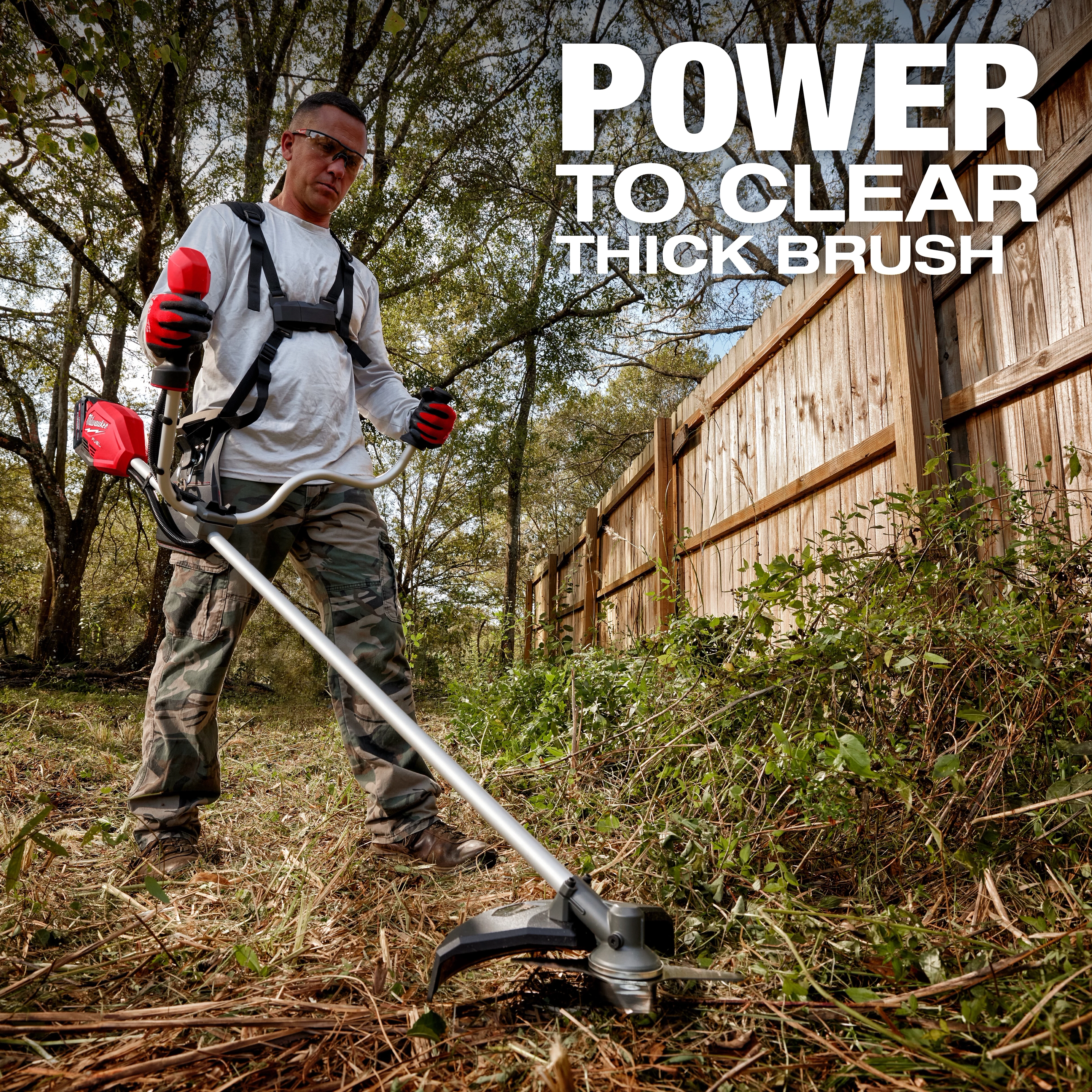 A person using the M18 FUEL™ Brush Cutter to clear thick brush along a wooden fence line in a wooded area. Text on the image reads, "POWER TO CLEAR THICK BRUSH."