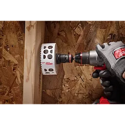 A gloved hand using a power drill with a 3/8" QUIK-LOK™ Arbor Set is shown drilling a hole in a piece of wood attached to an OSB board.