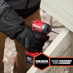 Heated Winter Gloves using Hexon Heat Technology are worn by a person indoors while operating a red Milwaukee power drill, screwing into a wooden surface. Gloves are black with a branding logo, providing warmth and dexterity for winter tasks. Text reads "Stays Warmer for Longer" in a badge.