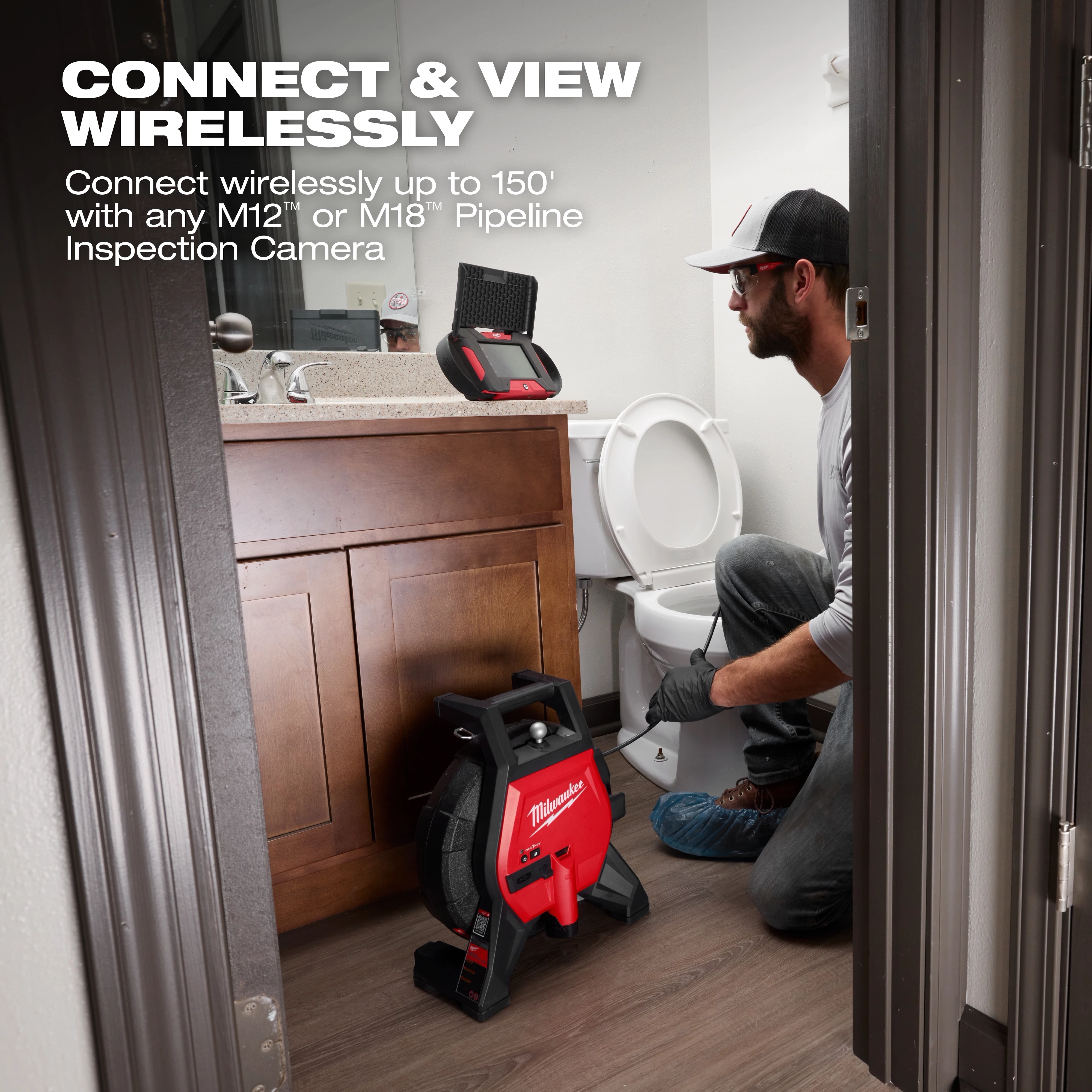 A person is kneeling in a bathroom beside a toilet, working with a Milwaukee pipeline inspection camera. The camera equipment is on the floor, and a monitor is on the sink. Text on the image advertises wireless connection up to 150 feet with M12 or M18 pipeline inspection cameras.