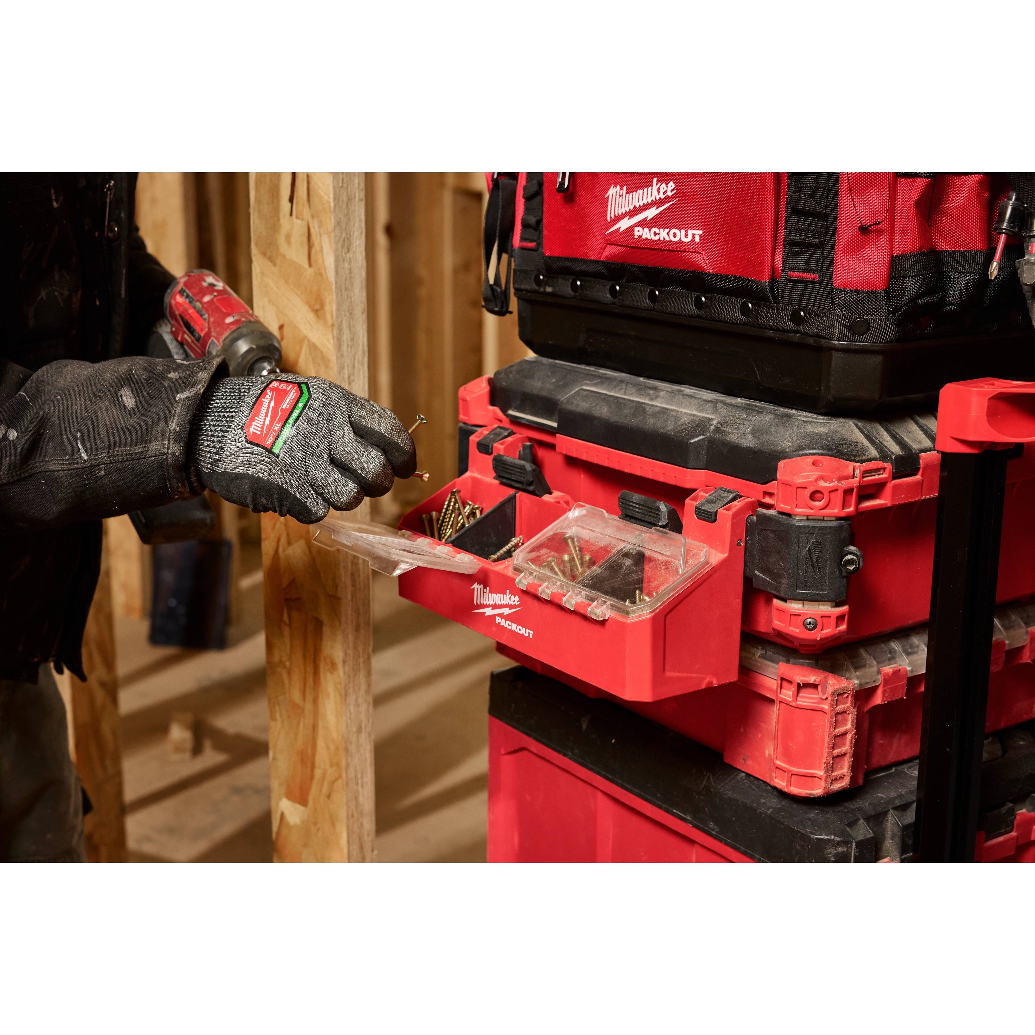 A person wearing work gloves uses the PACKOUT Tool Box 2-Bin Attachment to organize screws, shown attached to a red tool storage system.