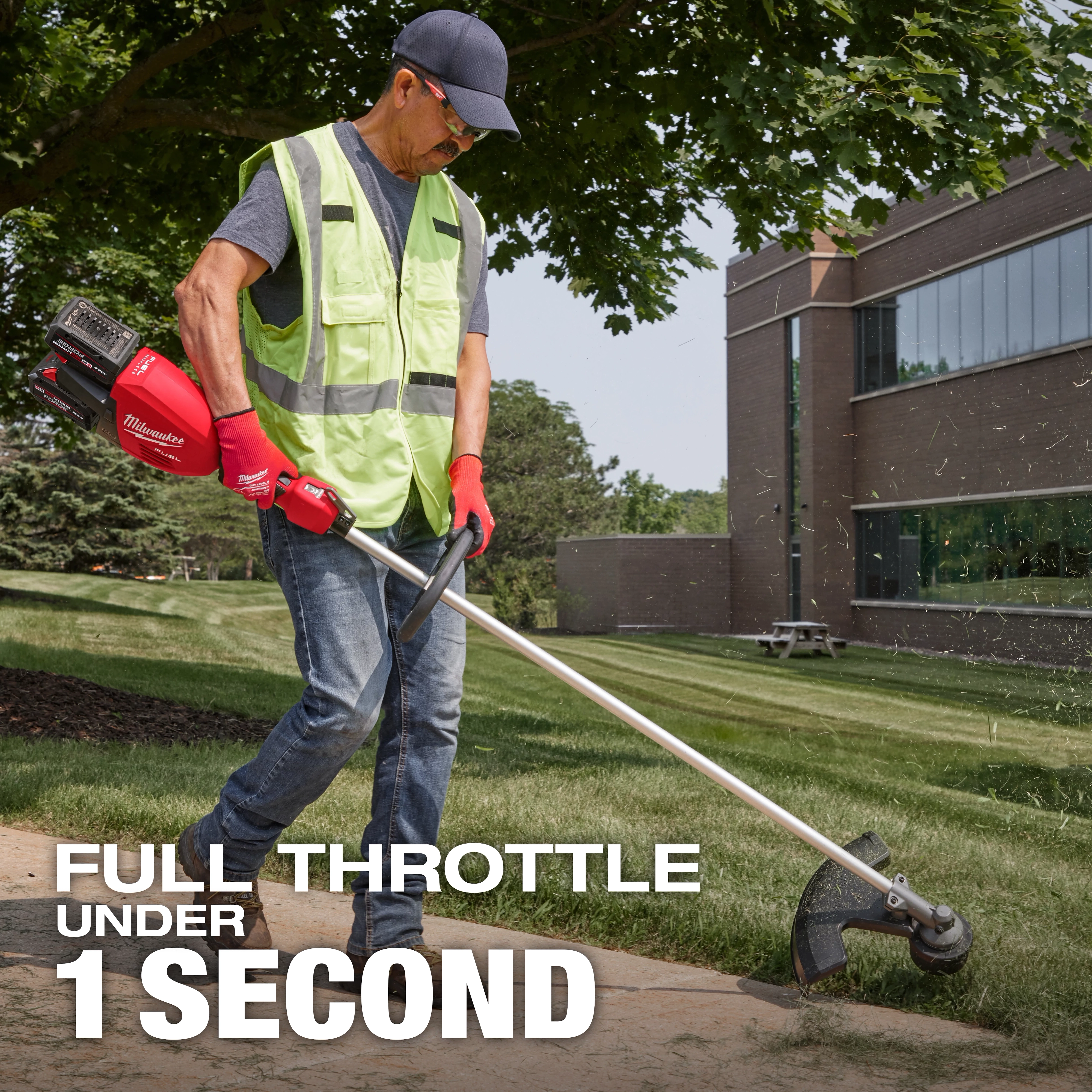 A person wearing a high-visibility vest and red gloves is using a Milwaukee grass trimmer on a lawn. In the background is a modern building. The text reads, "Full throttle under 1 second."