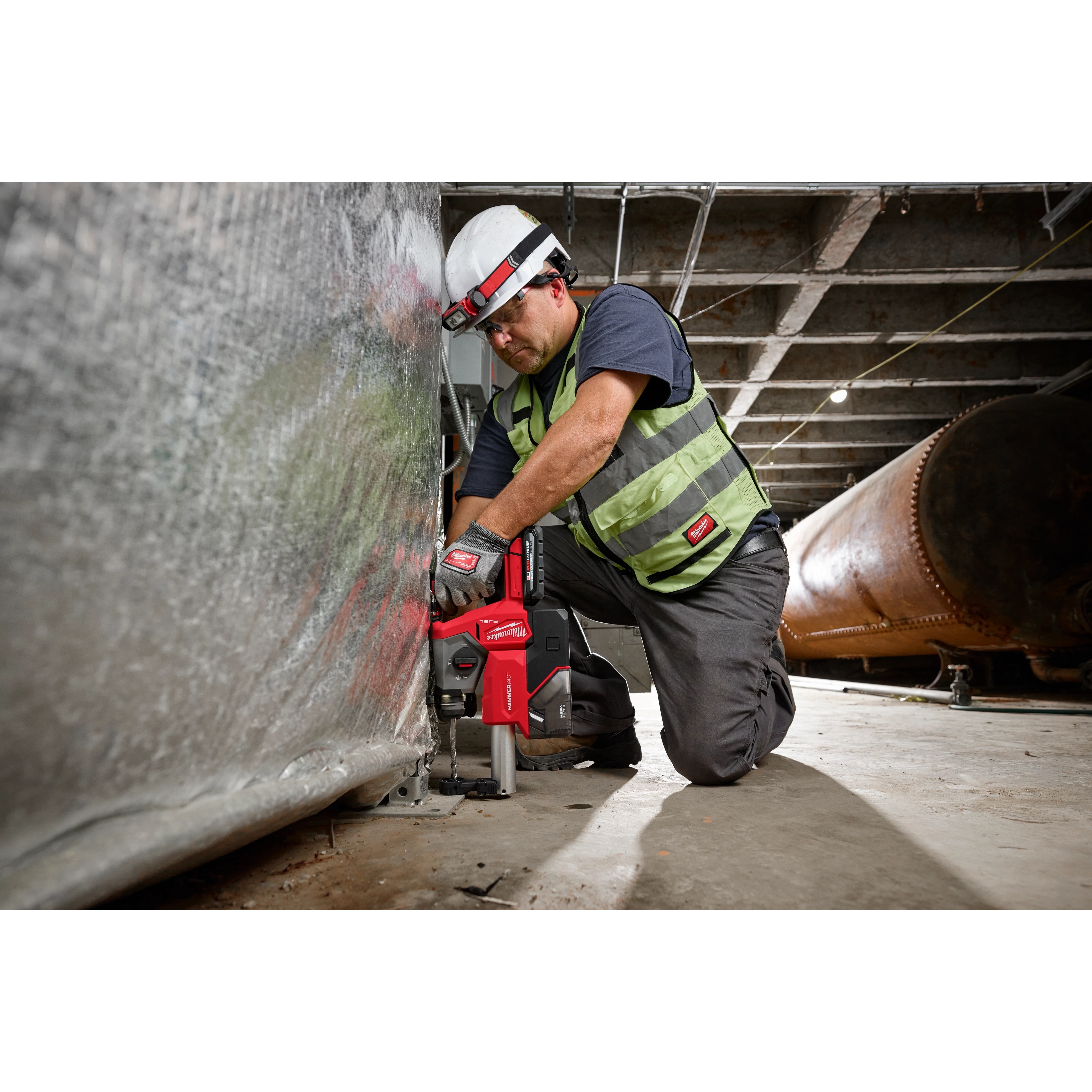 A worker in safety gear uses an M18 FUEL™ 5/8" SDS Plus Rotary Hammer with Dust Extractor Kit to drill into a metal surface inside an industrial setting.