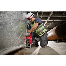 A worker in safety gear uses an M18 FUEL™ 5/8" SDS Plus Rotary Hammer with Dust Extractor Kit to drill into a metal surface inside an industrial setting.