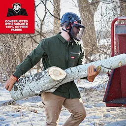 Person carrying a large log outdoors while wearing a GRIDIRON Flannel Shirt and safety helmet.