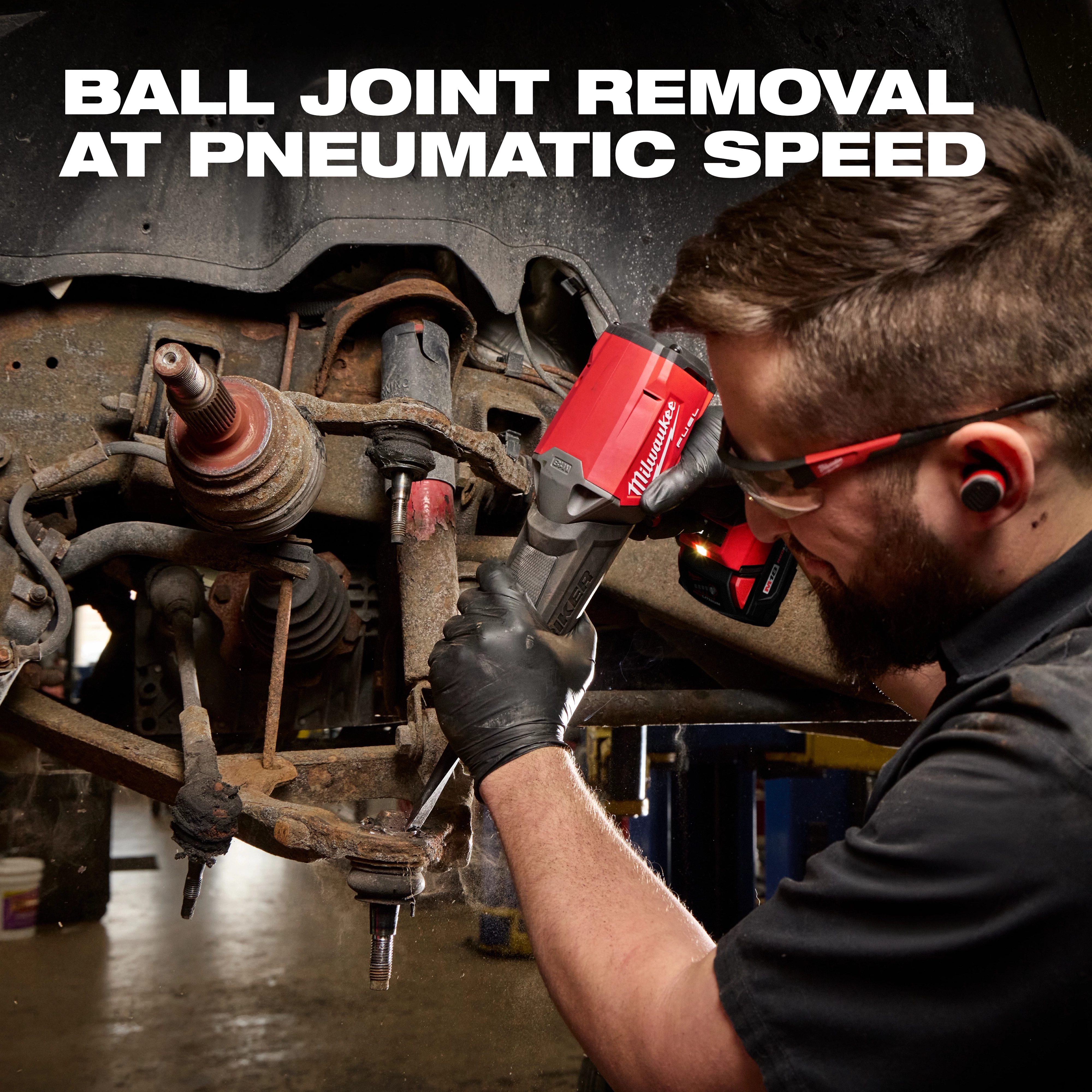 Worker using the red M18 FUEL STRIKER Hammer Chisel on a vehicle suspension assembly.