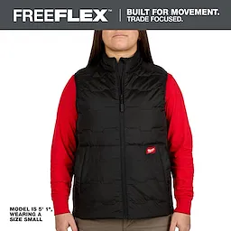 A model wearing a black Milwaukee Freeflex vest paired with a red long-sleeve shirt. The vest has a front zipper and a small red logo patch. The model's height is 5'1" and is wearing a size small.