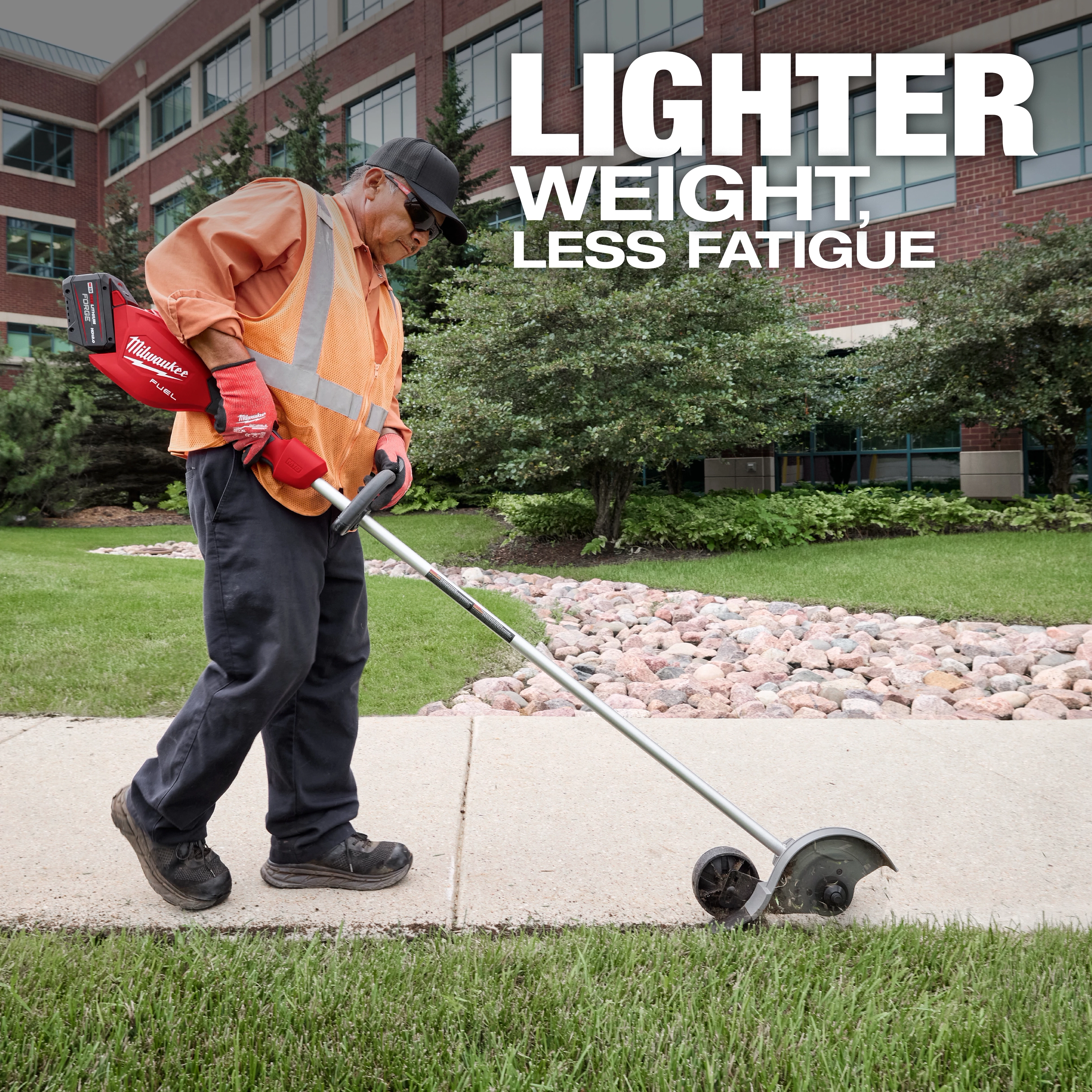 A worker in an orange vest and gloves uses an M18™ FUEL™ Edger on a sidewalk. The background shows a landscaped area with rocks, greenery, and a brick building. Text reads, "LIGHTER WEIGHT, LESS FATIGUE."