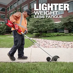 A worker in an orange vest and gloves uses an M18™ FUEL™ Edger on a sidewalk. The background shows a landscaped area with rocks, greenery, and a brick building. Text reads, "LIGHTER WEIGHT, LESS FATIGUE."