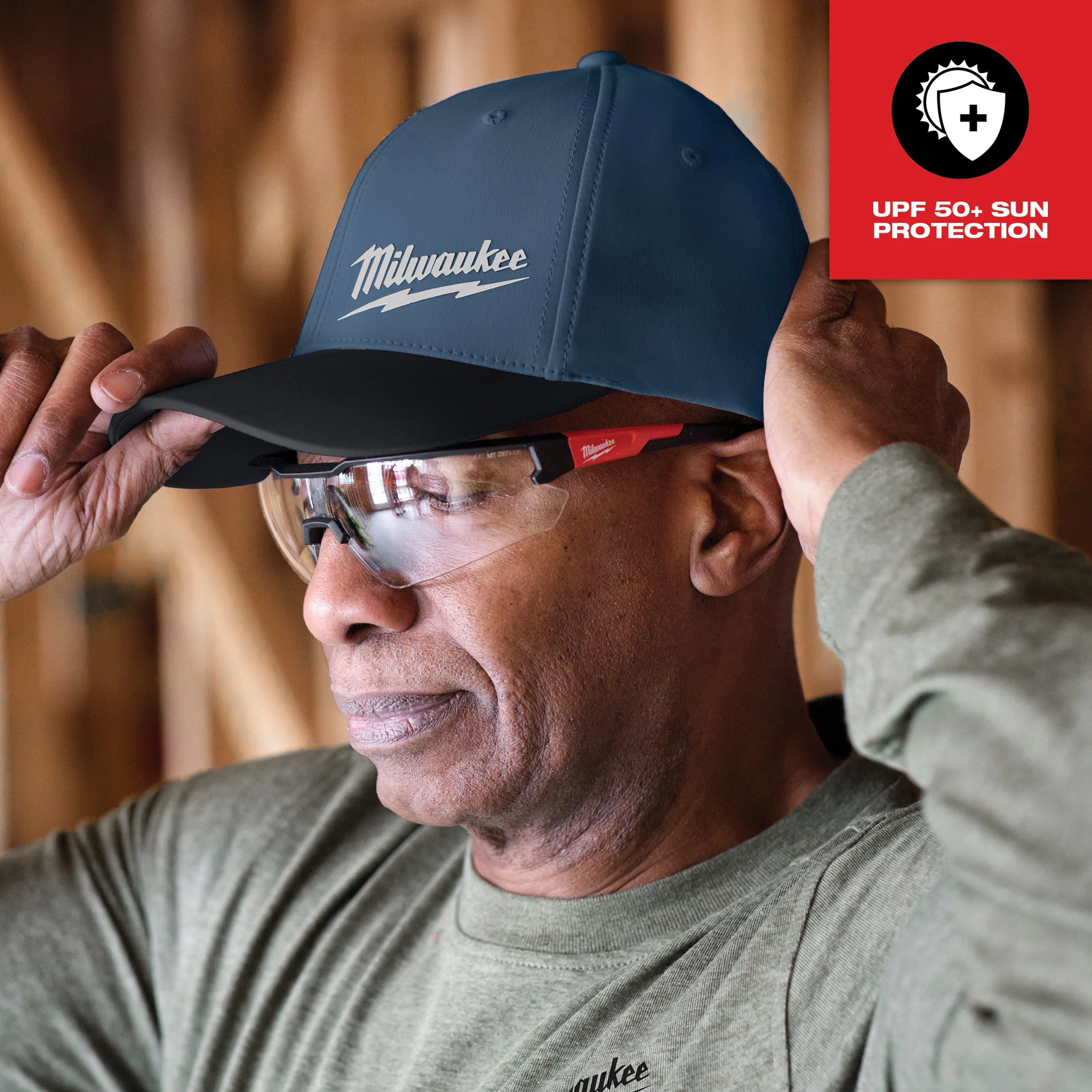 Man wearing a Workskin Performance Fitted Hat - Blue Feature Shot 2 with UPF 50+ sun protection, adjusting the cap's brim.
