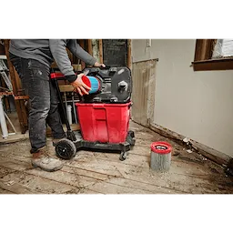 Person replacing the filter in a red Large Wet/Dry Vacuum High Efficiency Filter on a construction site with wooden floors.