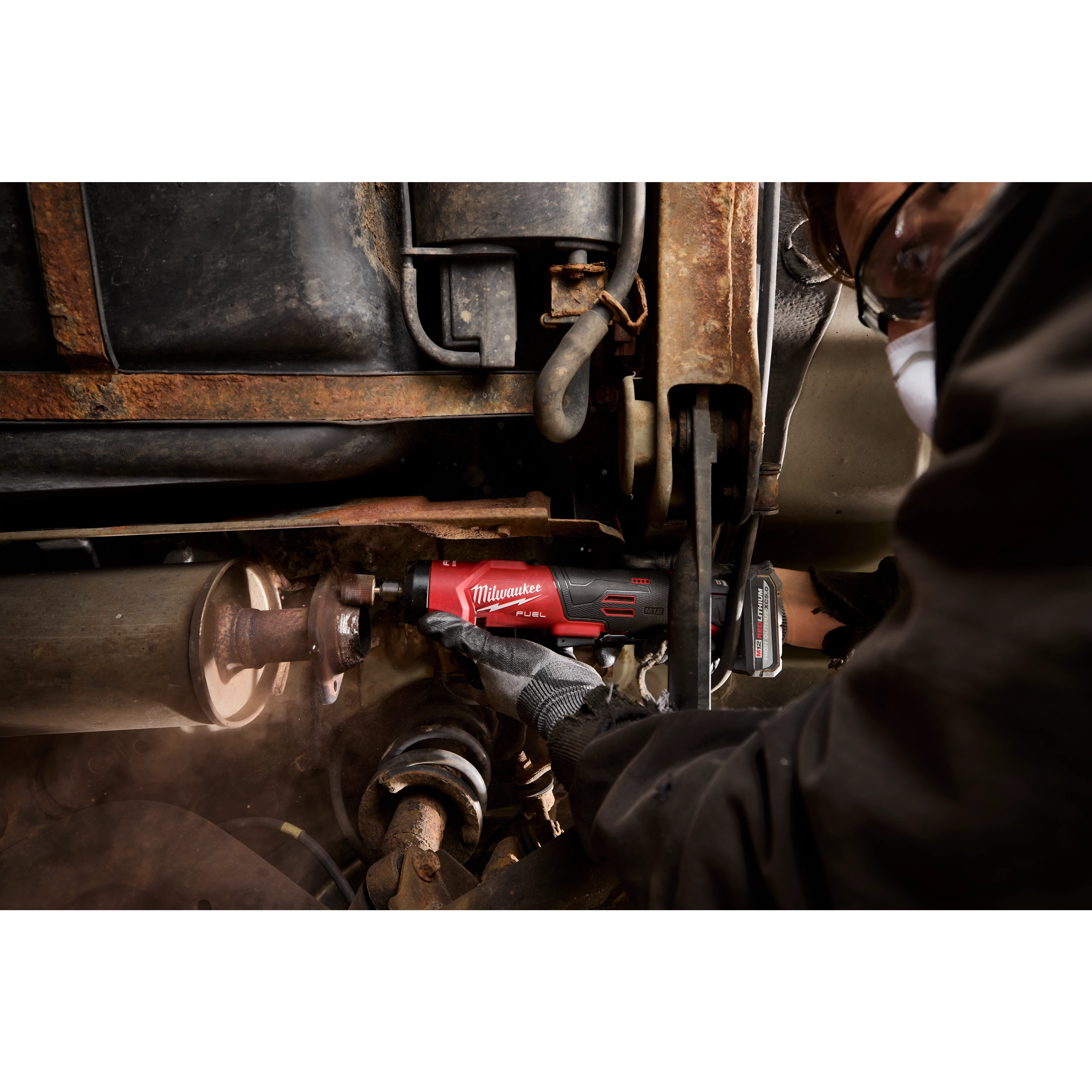 M12 FUEL 1/4" Straight Die Grinder being used on metal parts under a vehicle chassis.