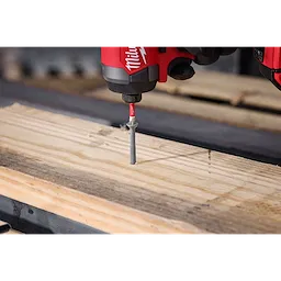 A close-up of a red power drill driving a screw into a piece of wood using the SHOCKWAVE™ 2” Impact Phillips #3 Power Bit. The drill is shown in action, firmly holding and maneuvering the screw into the plank.