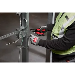 A person wearing gloves holds a 10-24 AWG Compact Comfort Grip Wire Stripper & Cutter while working on electrical wiring attached to a metal frame.
