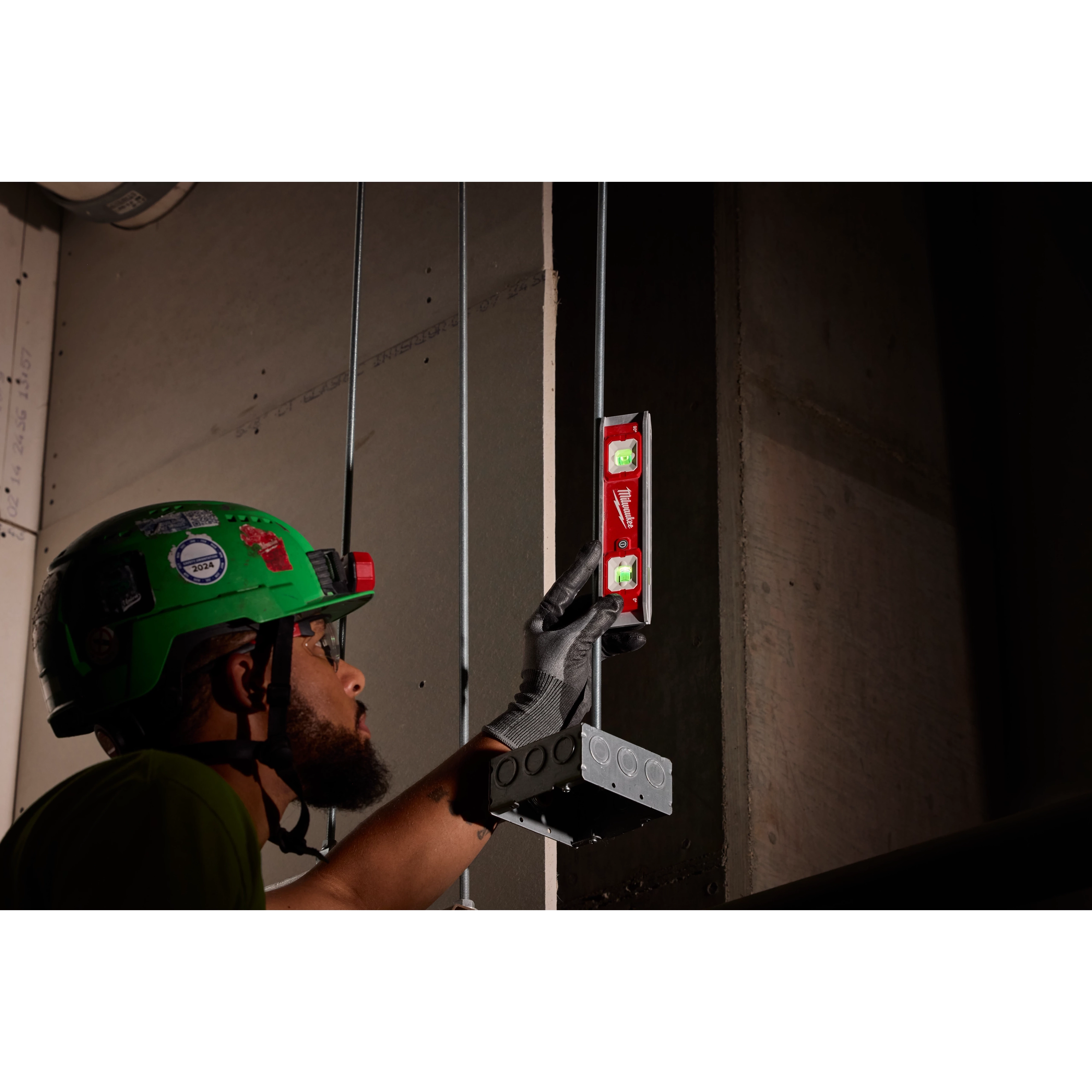 A person wearing protective gear uses a 9" Torpedo Level with Lighted Vials to align an electrical box on a wall.