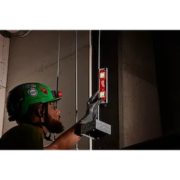 A person wearing protective gear uses a 9" Torpedo Level with Lighted Vials to align an electrical box on a wall.