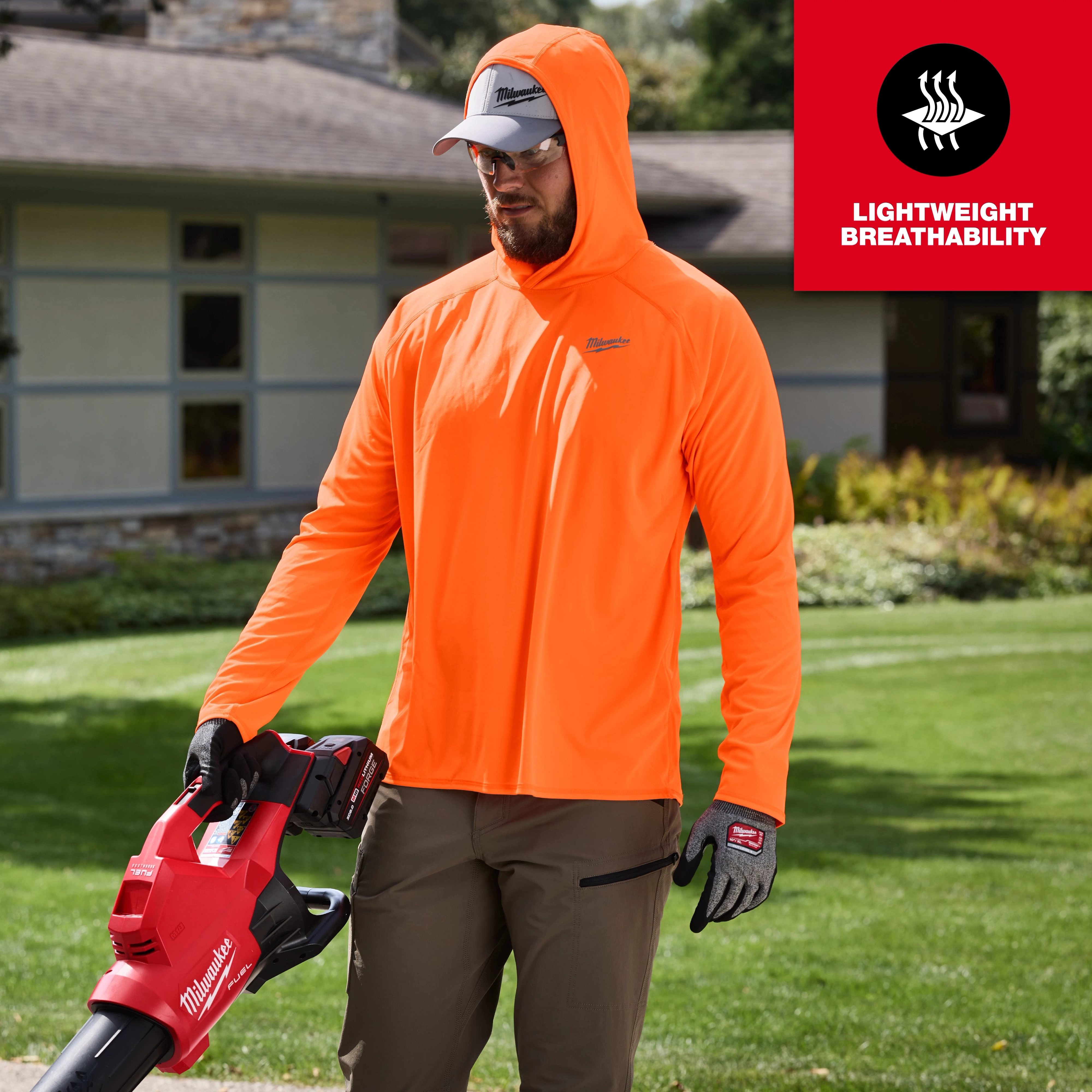 A person wearing an orange WORKSKIN Hooded Sun Shirt is standing on grass, holding a Milwaukee leaf blower. The shirt is noted for its lightweight breathability, indicated by the text and symbol in the upper right corner.