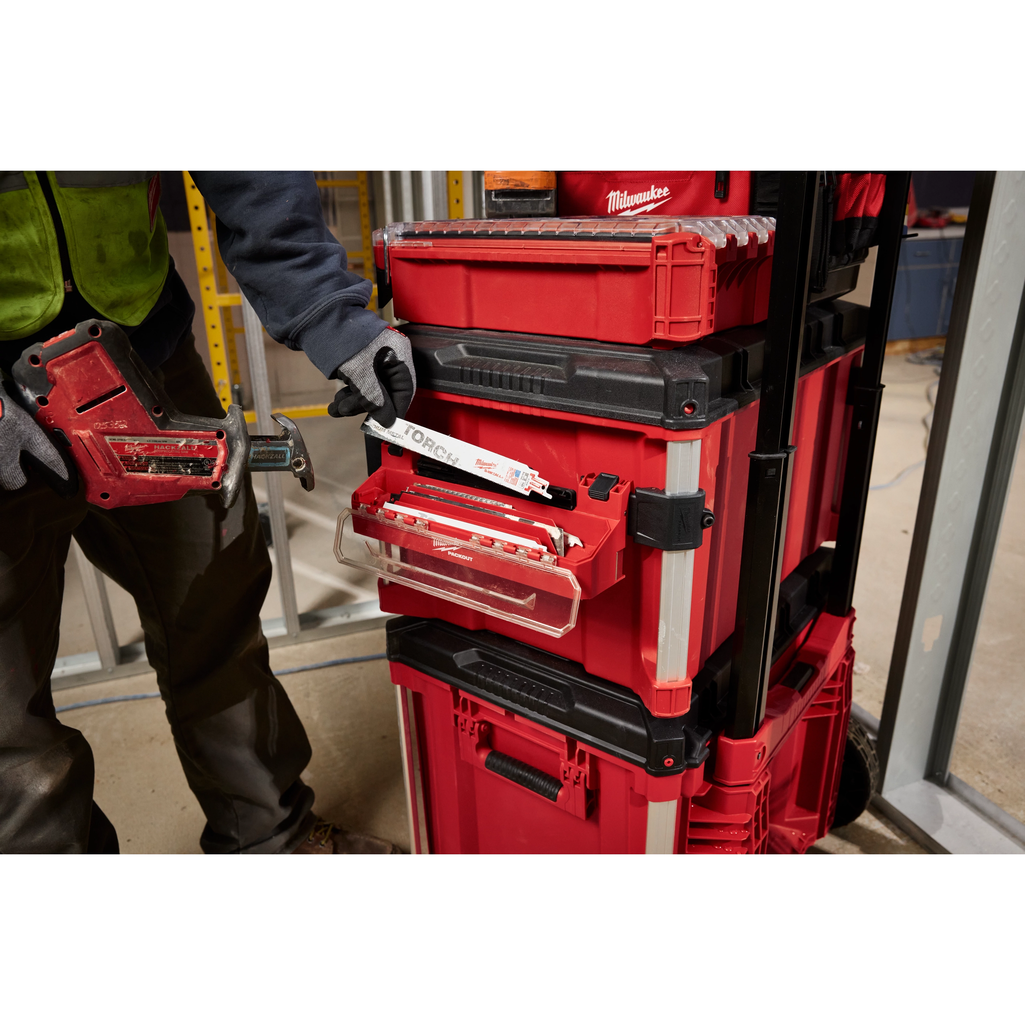 Person using a PACKOUT Tool Box Accessory Case Attachment with red modular toolboxes on a construction site.