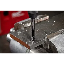 The 1/2"-13 NC Straight Flute Plug Tap is shown in use, mounted on a drill press and creating threads in a metal plate clamped in a vise. Metal shavings are visible around the freshly tapped hole.