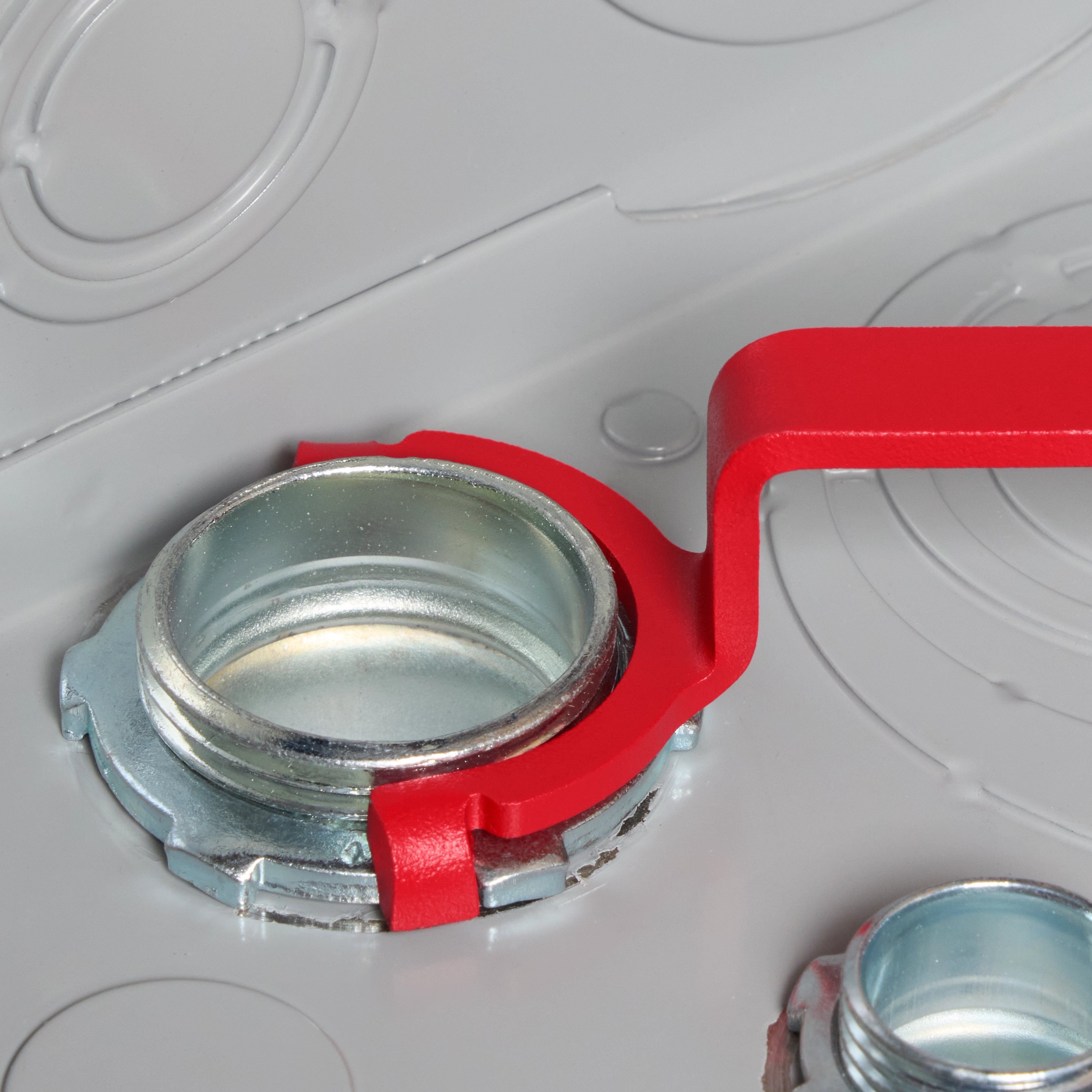 A red-handled wrench from the 3 PC Locknut Wrench Set is shown tightening a metal locknut on a grey surface. A smaller locknut is visible in the foreground, and another locknut can be seen partially to the right.