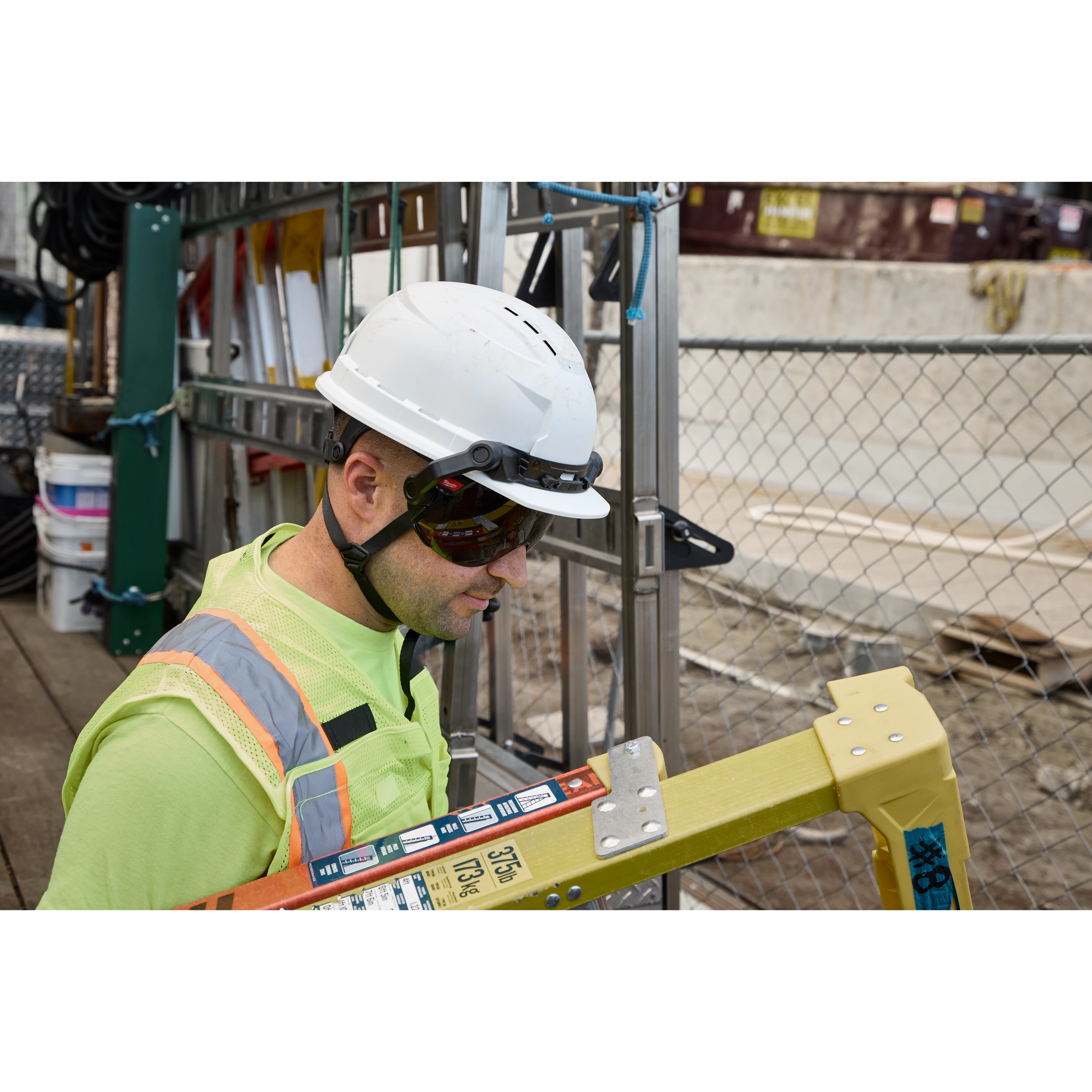 Worker wearing a BOLT 4PT White Front Brim Vented Safety Helmet - Type 2, Class C, holding a ladder.