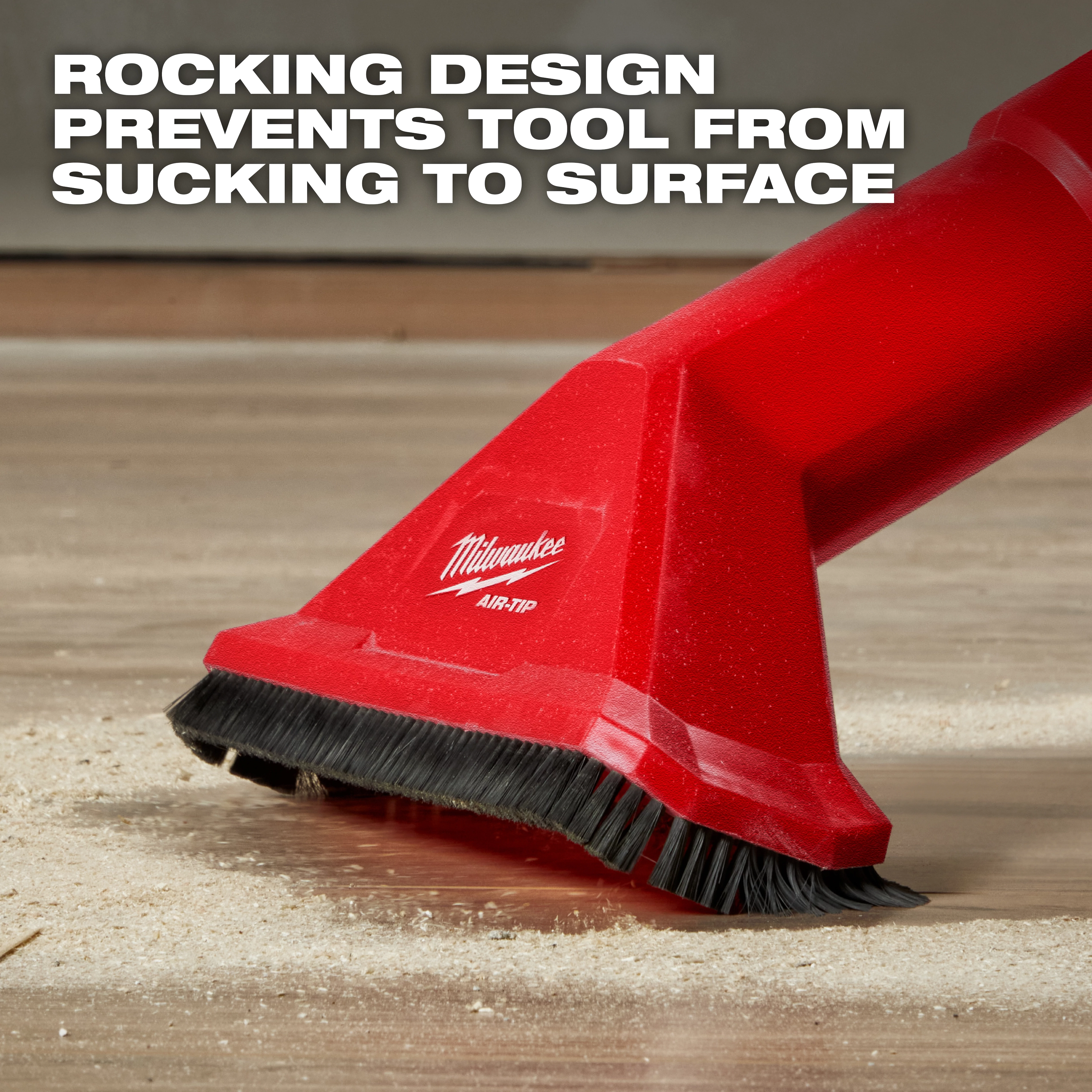 Image of the AIR-TIP™ 2-1/2" Rocking Utility Nozzle w/ Brushes. The red nozzle has an integrated brush and the text reads, "ROCKING DESIGN PREVENTS TOOL FROM SUCKING TO SURFACE." The nozzle is shown on a wooden floor with some debris around it.