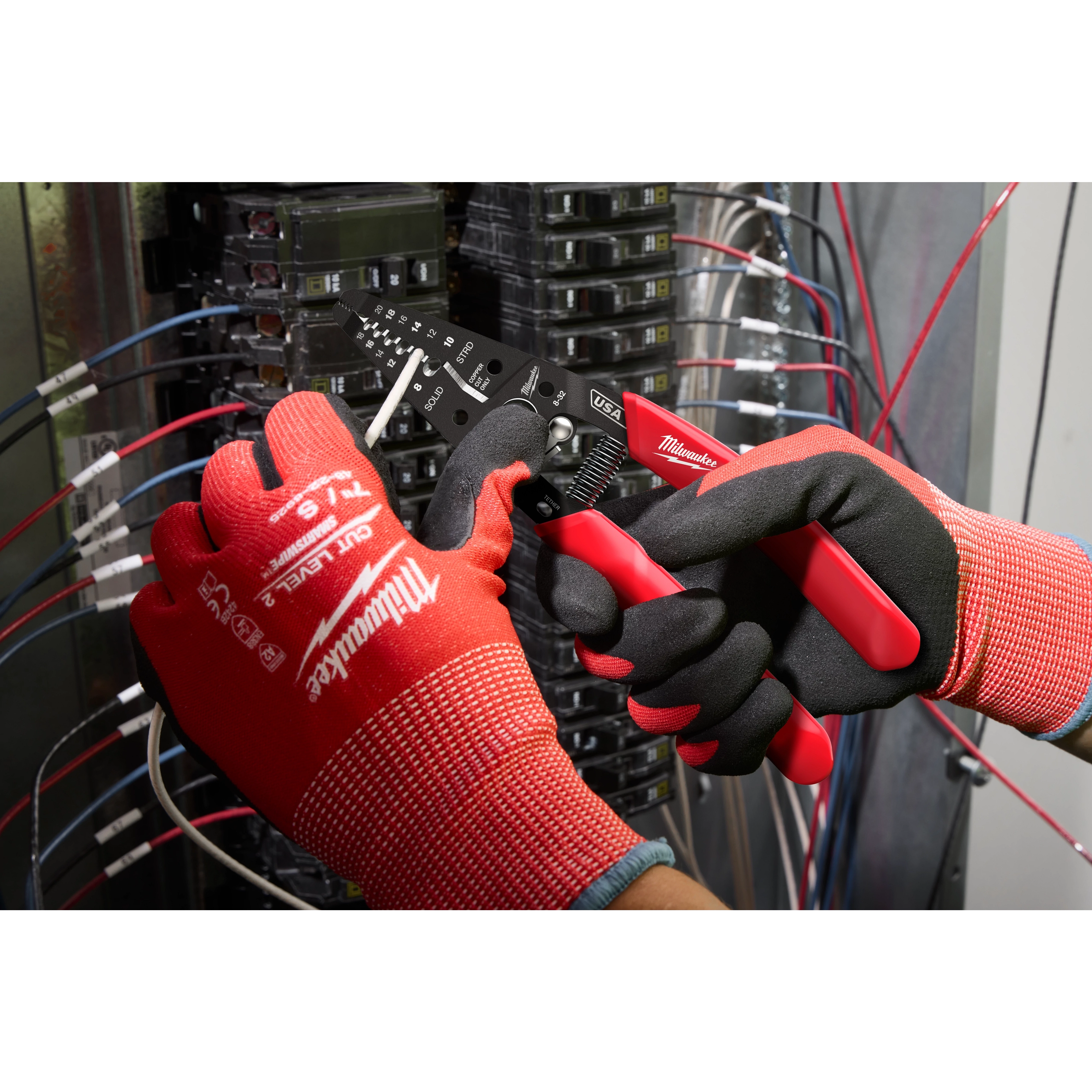 A technician uses the 8-20 AWG Dipped Grip Wire Stripper & Cutter (USA) to strip a wire in an electrical panel. The tool features dipped grips for comfort and multiple cutting and stripping holes. The technician wears red and black gloves while working with the wires.