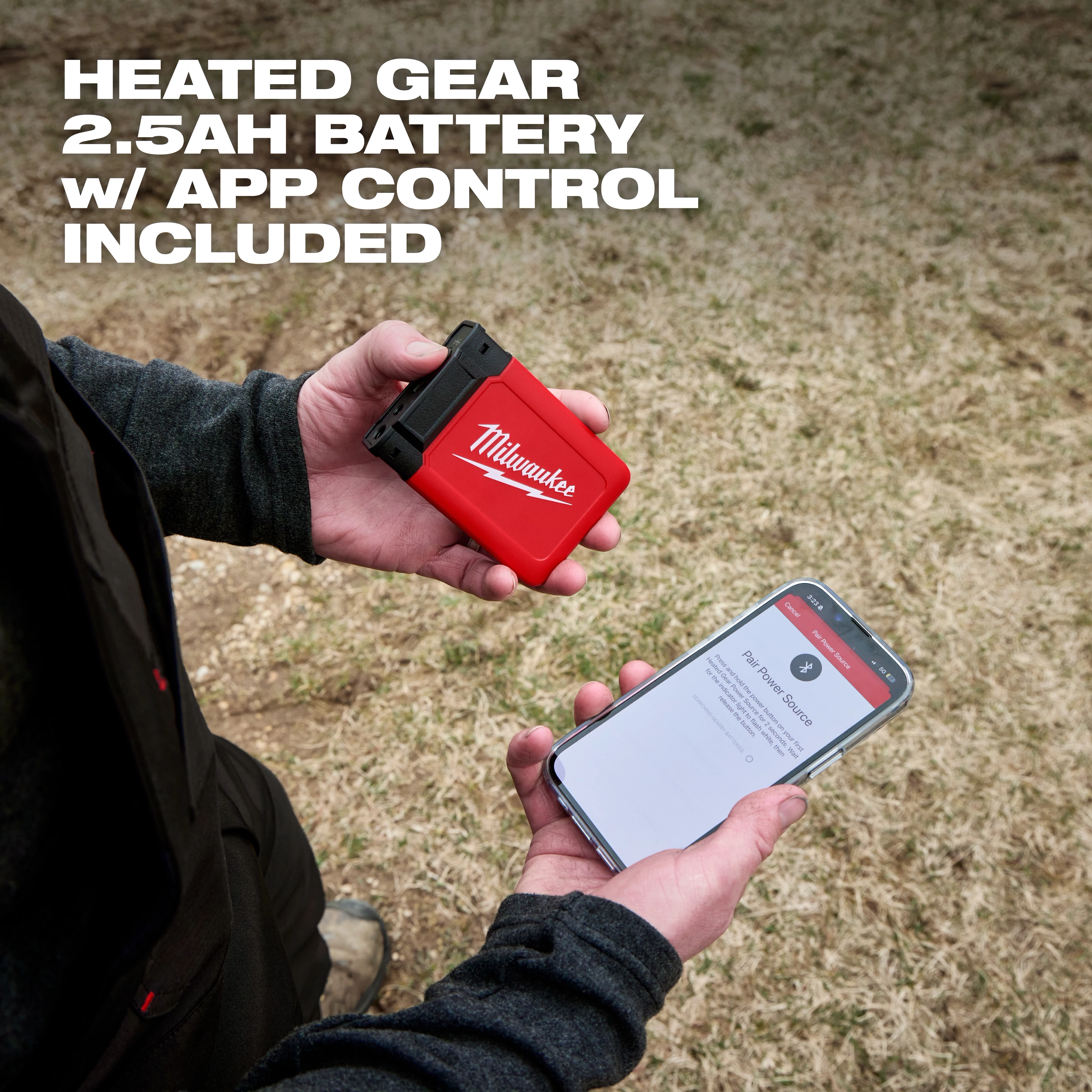 Hands hold a Milwaukee heated gear battery and phone, promoting Milwaukee Heated Merino Wool Crew Neck Baselayer and Baselayer Pants.