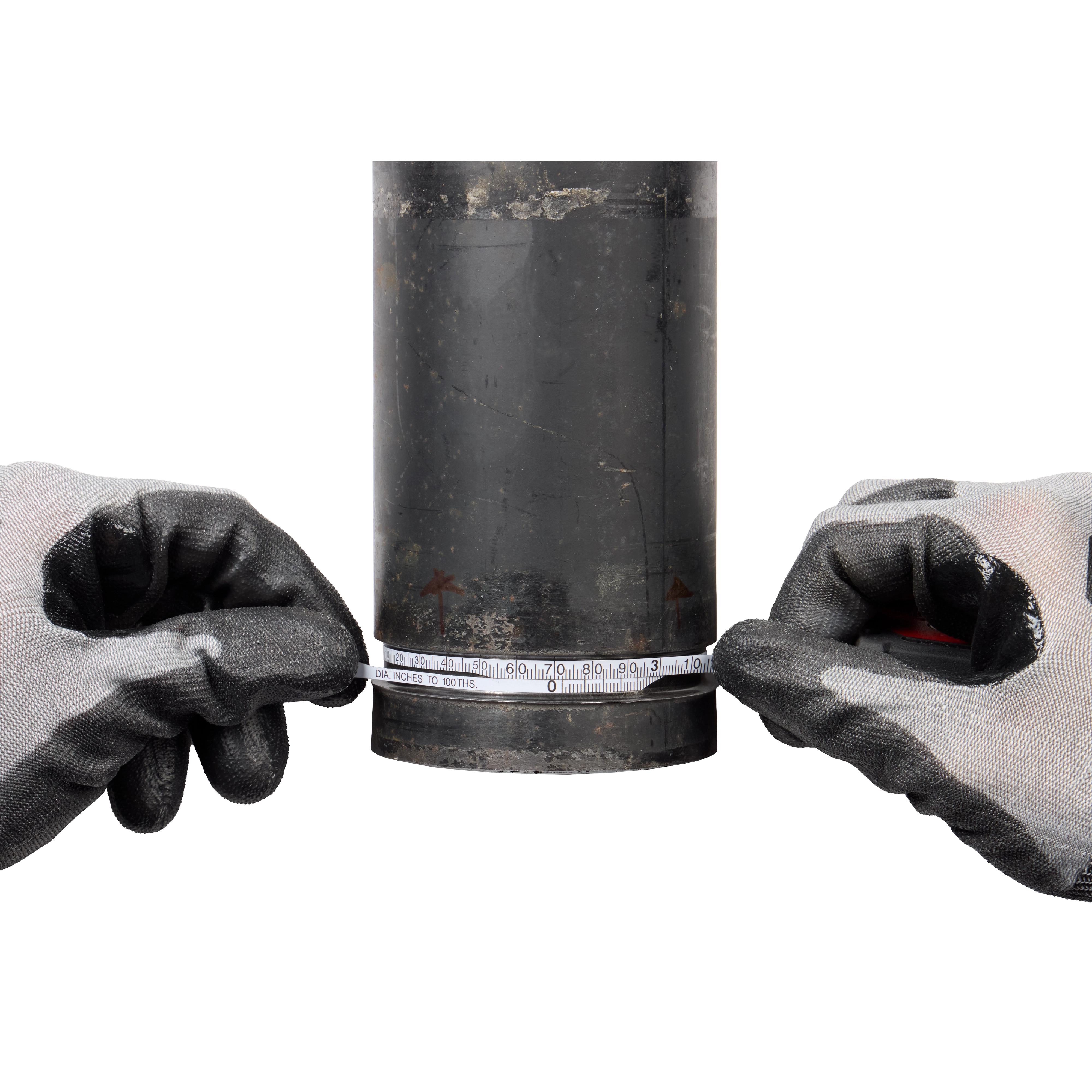 Gloved hands are using a Pipe Diameter Tape Measure to measure the circumference of a dark cylindrical pipe. The tape measure displays both metric and imperial units.