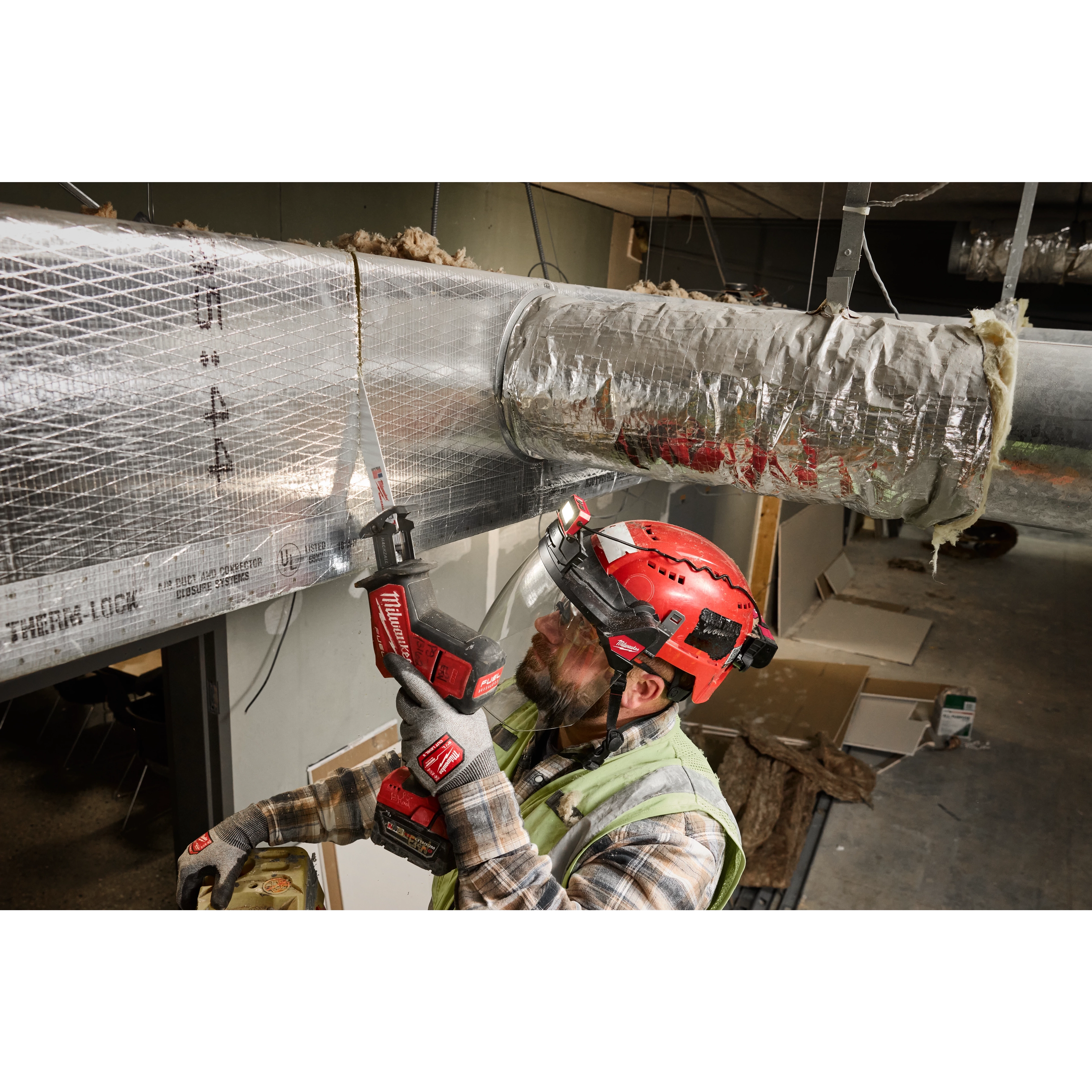 A construction worker wearing a red helmet and safety vest is using a power tool on HVAC ductwork. He is protected by the BOLT™ Gasketed Full Face Shield - Clear Dual Coat Lens, which is compatible with Milwaukee® BOLT™ Safety Helmets & BOLT™ Hard Hats.
