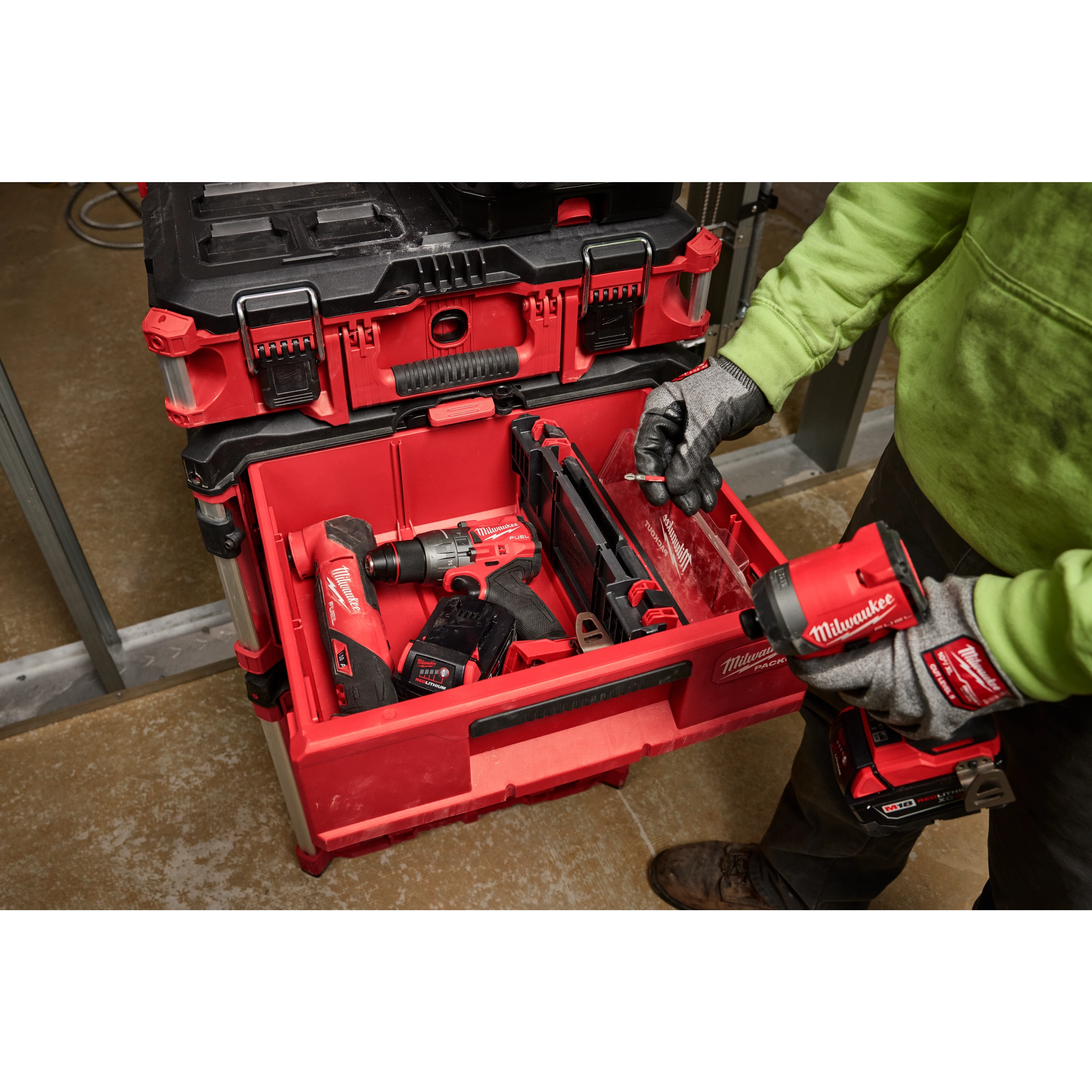 Person organizing power tools in a red Divider for PACKOUT Drawer Tool Boxes with black latches. Wearing green hoodie and gloves.