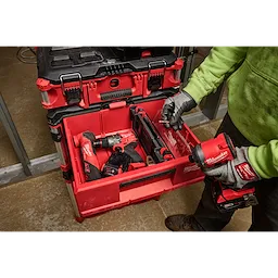Person organizing power tools in a red Divider for PACKOUT Drawer Tool Boxes with black latches. Wearing green hoodie and gloves.