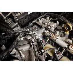 A person wearing a black glove uses a 3/8" Drive 4mm Long Hex Bit Socket attached to a ratchet wrench to work on an engine. The tool is being used to reach a bolt in a tight space within the car's engine compartment.