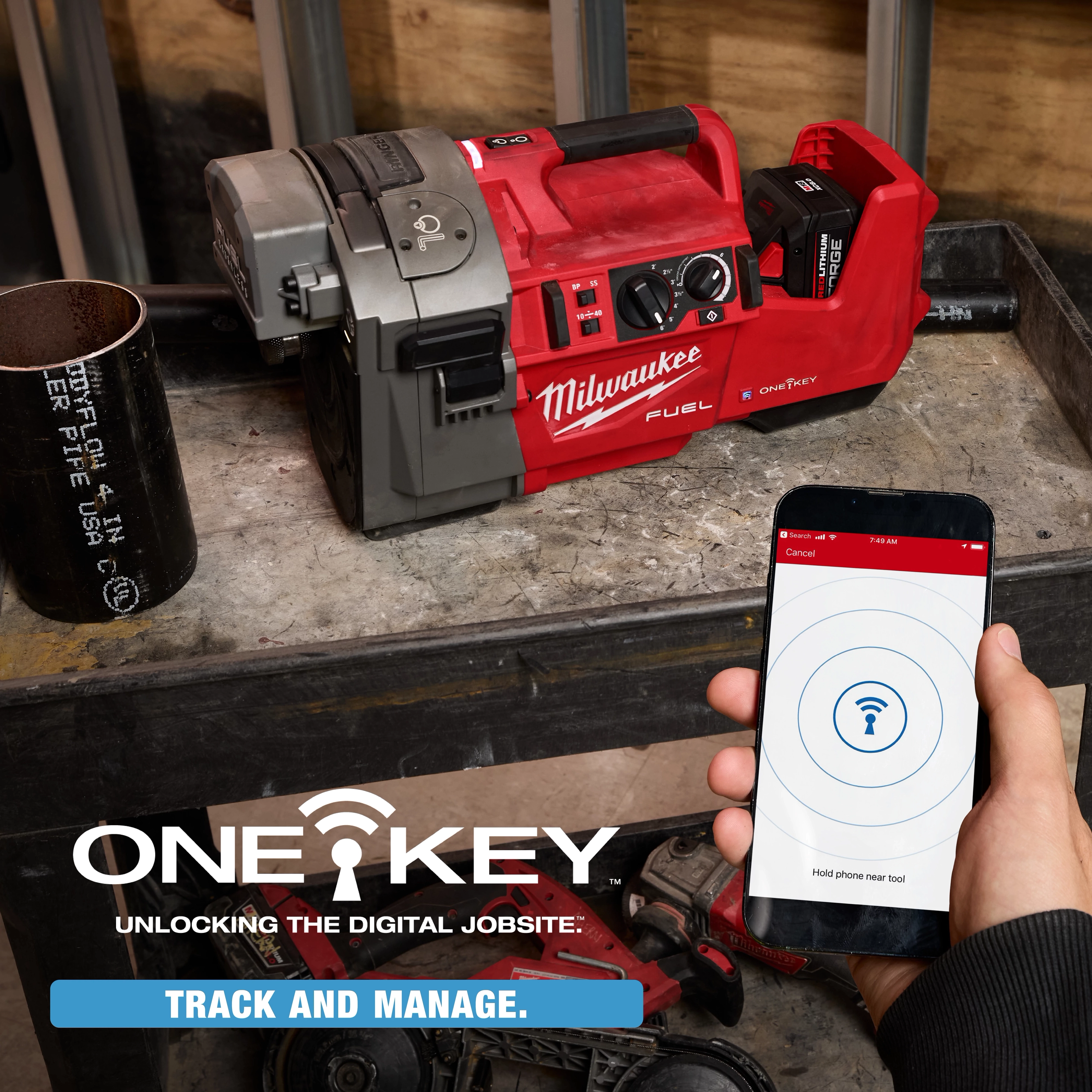 The image shows an M18 FUEL™ RINGER™ Roll Groover by Milwaukee placed on a workbench. A person is holding a smartphone with the ONE-KEY app screen visible, indicating tool tracking and managing. Text reads, "ONE-KEY - Unlocking the Digital Jobsite: Track and Manage."