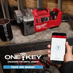 The image shows an M18 FUEL™ RINGER™ Roll Groover by Milwaukee placed on a workbench. A person is holding a smartphone with the ONE-KEY app screen visible, indicating tool tracking and managing. Text reads, "ONE-KEY - Unlocking the Digital Jobsite: Track and Manage."