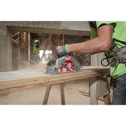 Worker using M18 FUEL 7-1/4" Rear Handle Circular Saw with ONE-KEY to cut wood on a construction site, wearing safety gear.