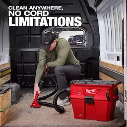 A person using the Milwaukee M18 FUEL NEXUS 6 Gallon Wet/Dry Vacuum w/ PACKOUT Compatibility & VACLINK inside a van. The red vacuum has a flexible hose, and text above reads, "CLEAN ANYWHERE, NO CORD LIMITATIONS."