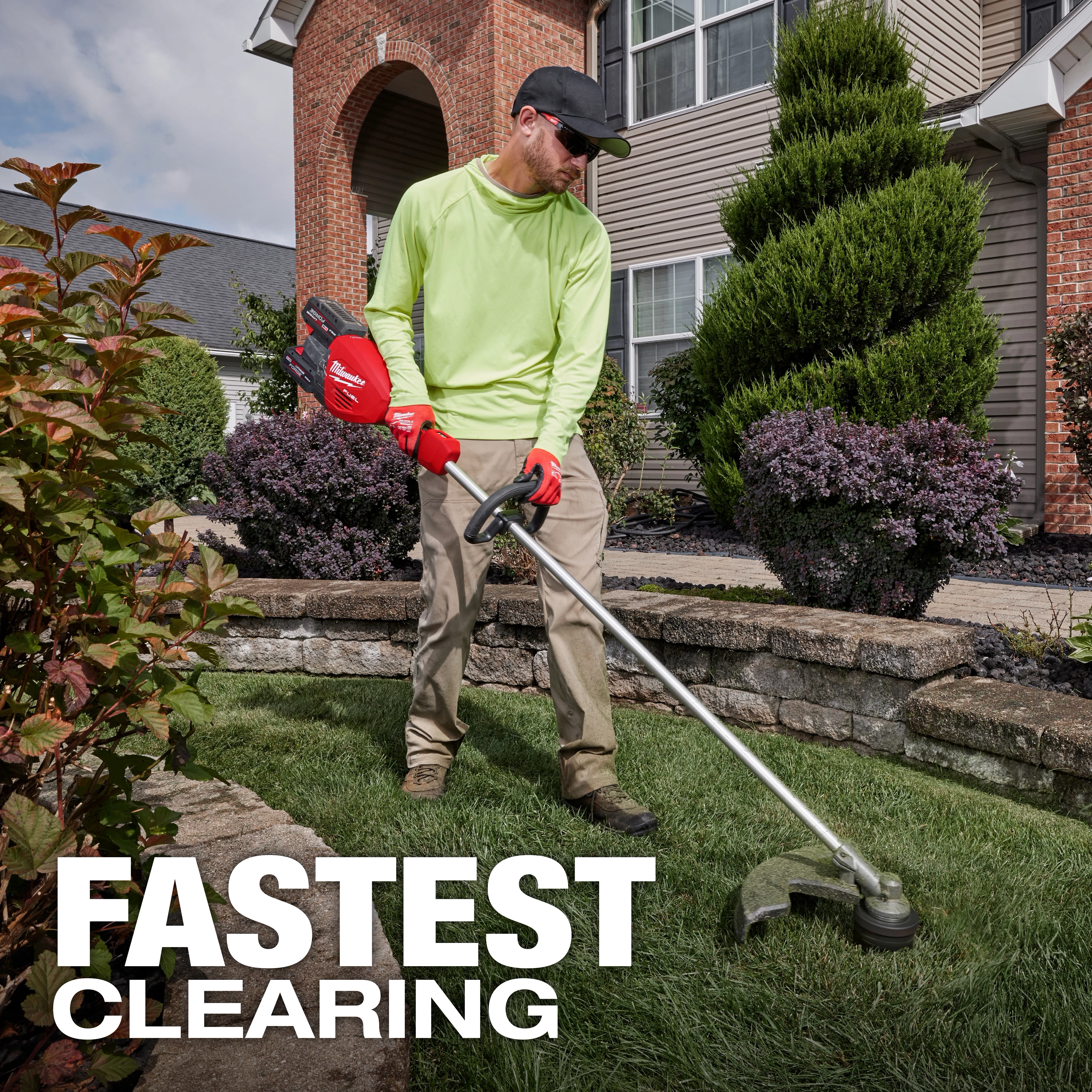 A person in a neon green long-sleeve shirt, tan pants, and a black cap uses a red Milwaukee string trimmer on a manicured lawn in front of a brick house with neatly trimmed bushes. Text overlay reads "FASTEST CLEARING" at the bottom of the image.