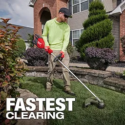 A person in a neon green long-sleeve shirt, tan pants, and a black cap uses a red Milwaukee string trimmer on a manicured lawn in front of a brick house with neatly trimmed bushes. Text overlay reads "FASTEST CLEARING" at the bottom of the image.