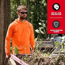 A person wearing an orange WORKSKIN Hooded Sun Shirt stands outdoors next to a wheelbarrow filled with branches. The shirt offers UPF 50+ sun protection and features odor-fighting fabric.