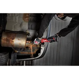 Worker using an M12 FUEL 1/4" Extended Die Grinder on rusted metal under a vehicle.