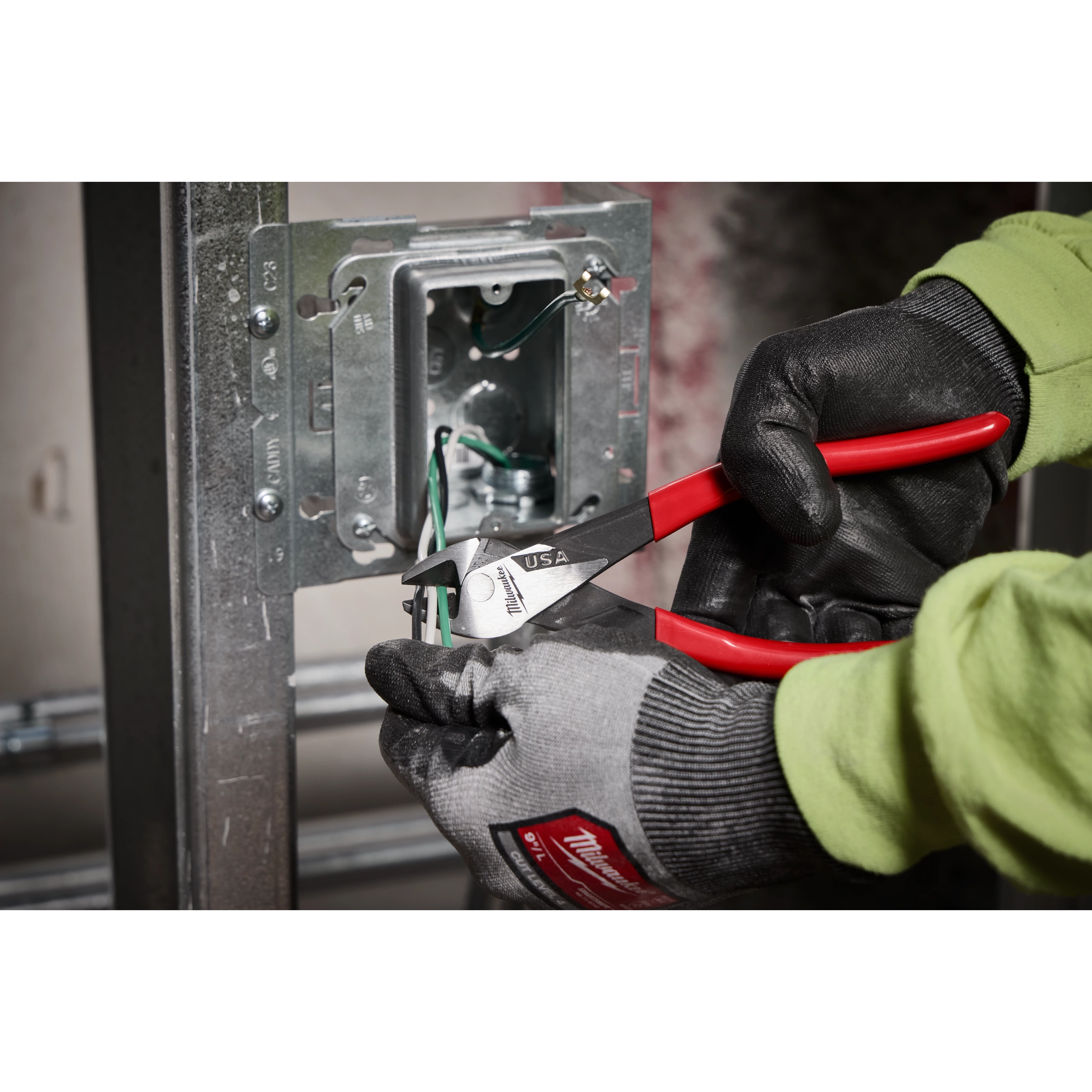 8" Angled Head Diagonal Dipped Grip Cutting Pliers (USA) are shown being used to cut wires inside an electric socket box. The pliers feature red handles and are held by a worker wearing black and grey gloves.
