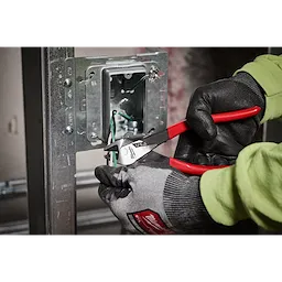 8" Angled Head Diagonal Dipped Grip Cutting Pliers (USA) are shown being used to cut wires inside an electric socket box. The pliers feature red handles and are held by a worker wearing black and grey gloves.