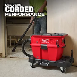 Milwaukee M18 FUEL™ NEXUS™ 6 Gallon Wet/Dry Vacuum w/ PACKOUT™ Compatibility & VACLINK™ is a red, portable vacuum cleaner on wheels, being used to clean a floor. The text "Delivers Corded Performance" is displayed in the upper-left corner.