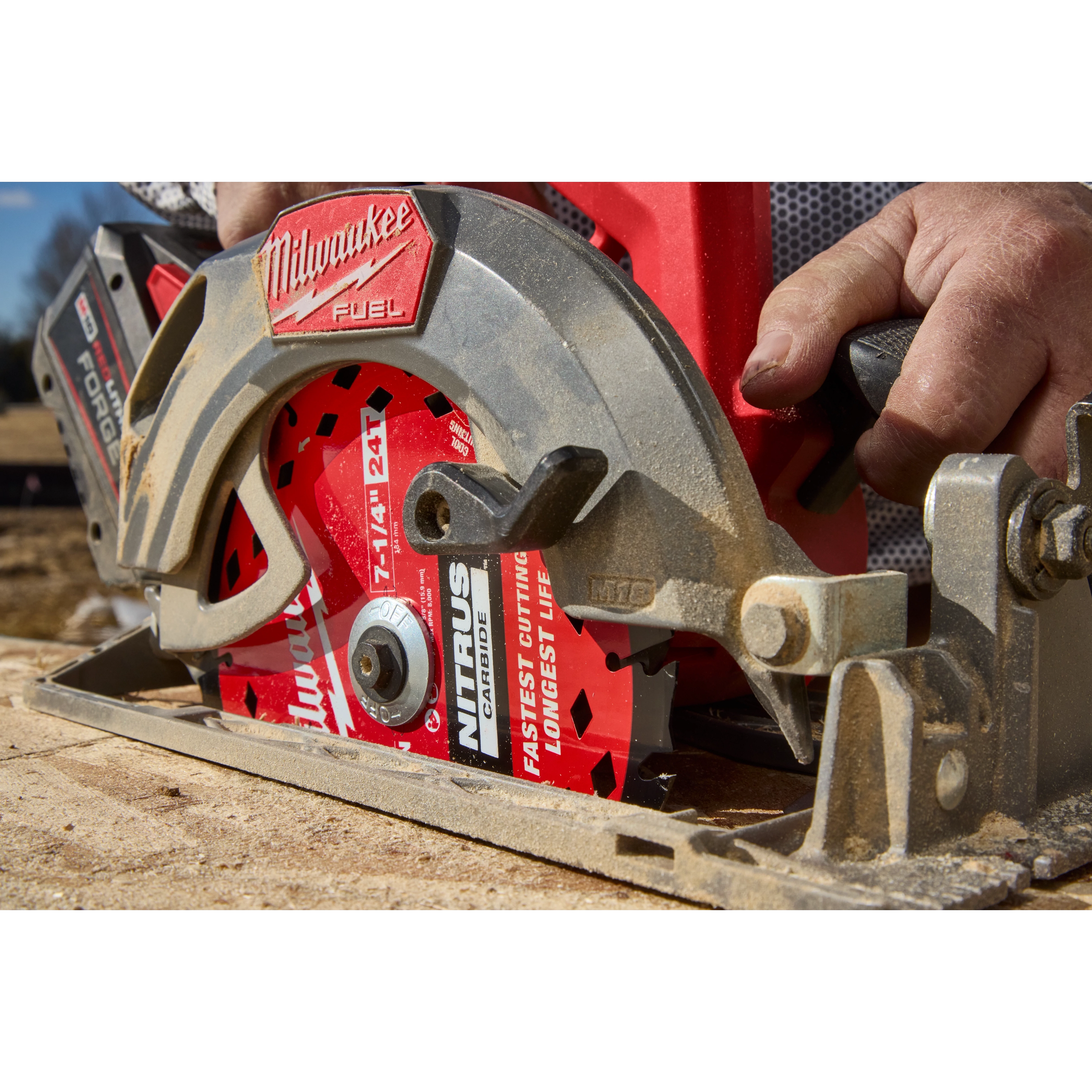 A Milwaukee Fuel circular saw is shown cutting wood, featuring the 7-1/4” 24T NITRUS™ Carbide Framing & Demolition Circular Saw Blade. A worker's hand is positioned on the saw's handle as it actively cuts through the material. The blade is red with branding and specifications visible.
