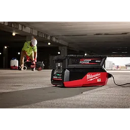 Milwaukee Rapid Charger on concrete floor, with a worker in safety gear using equipment in the background.