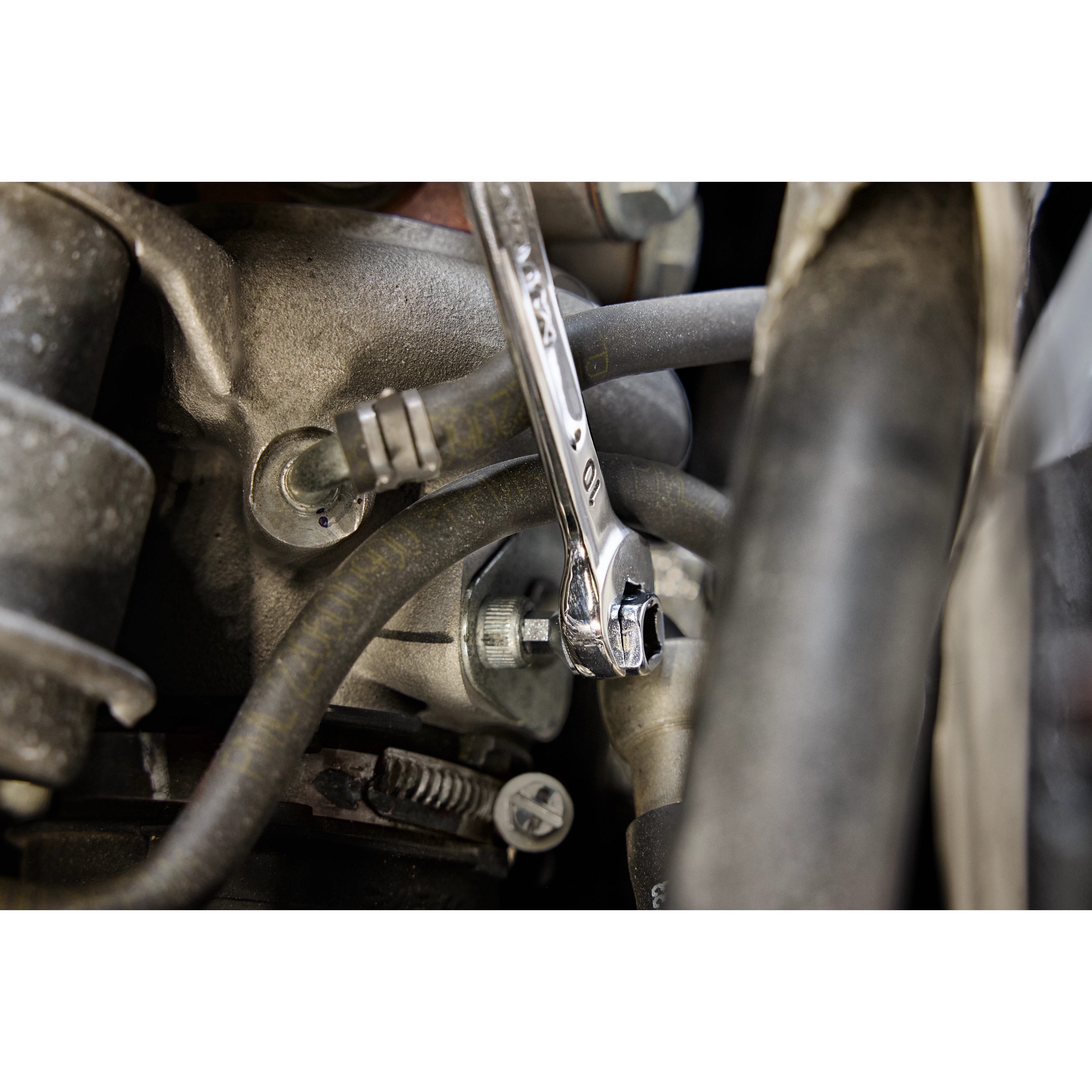A close-up image of a 10mm Milwaukee combination wrench being used to tighten a bolt in a mechanical assembly.