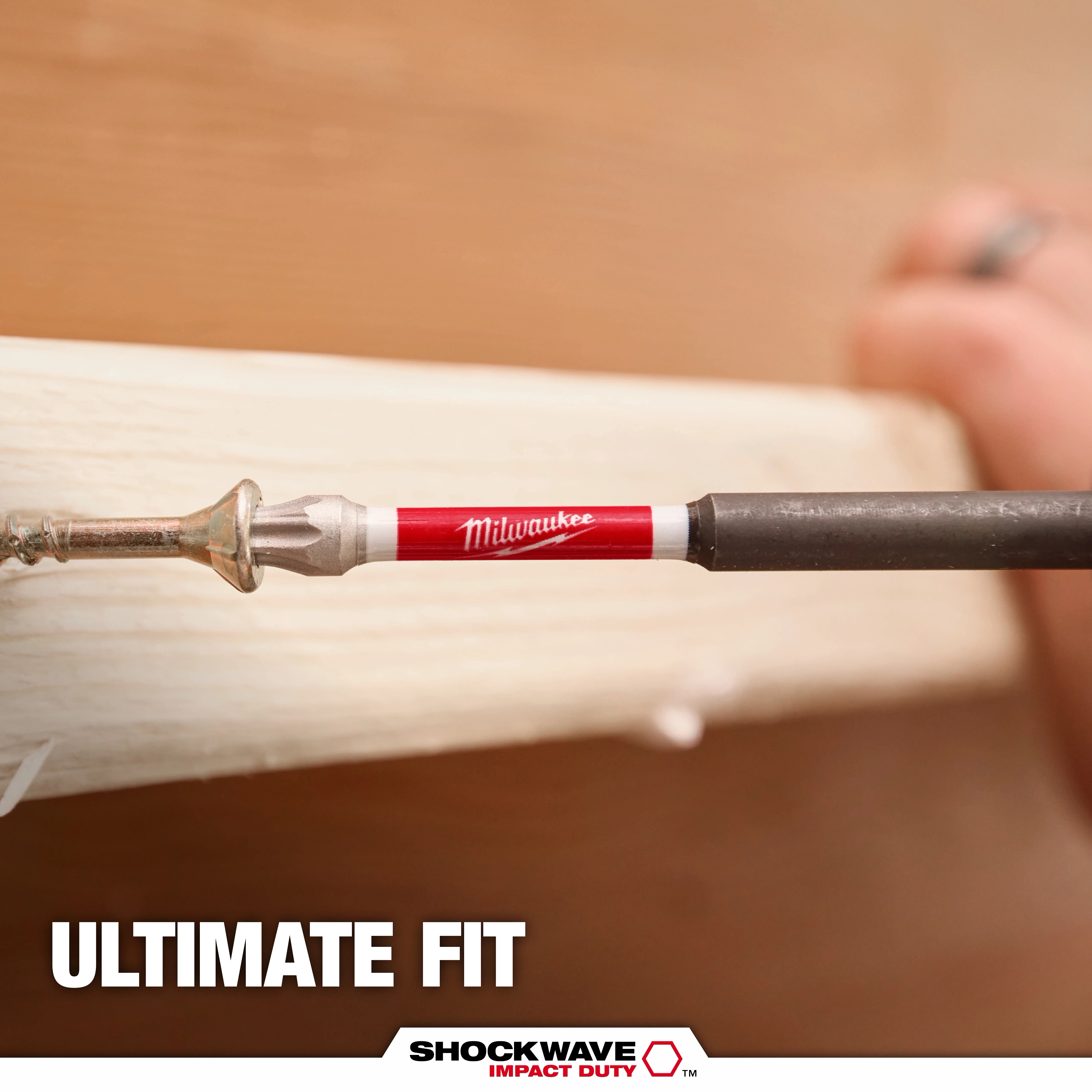 The image shows a Milwaukee SHOCKWAVE™ TORX® Bit being used to drive a screw into wood. The bit has a red and white shaft with the Milwaukee logo. The text "ULTIMATE FIT" and the SHOCKWAVE™ logo are displayed below.
